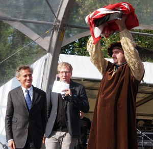 Bürgermeister und Hanse-Vormann Bernd Saxe, NDR-Moderator Jan Malte Andresen und Viljandis Bürgermeister Ando Kiviberg, der die Hanse-Fahne zeigt.